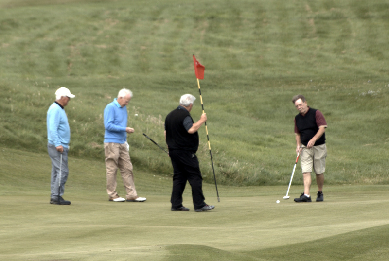 John McArthur holds the flag as others try to match his birdie on the 14th.